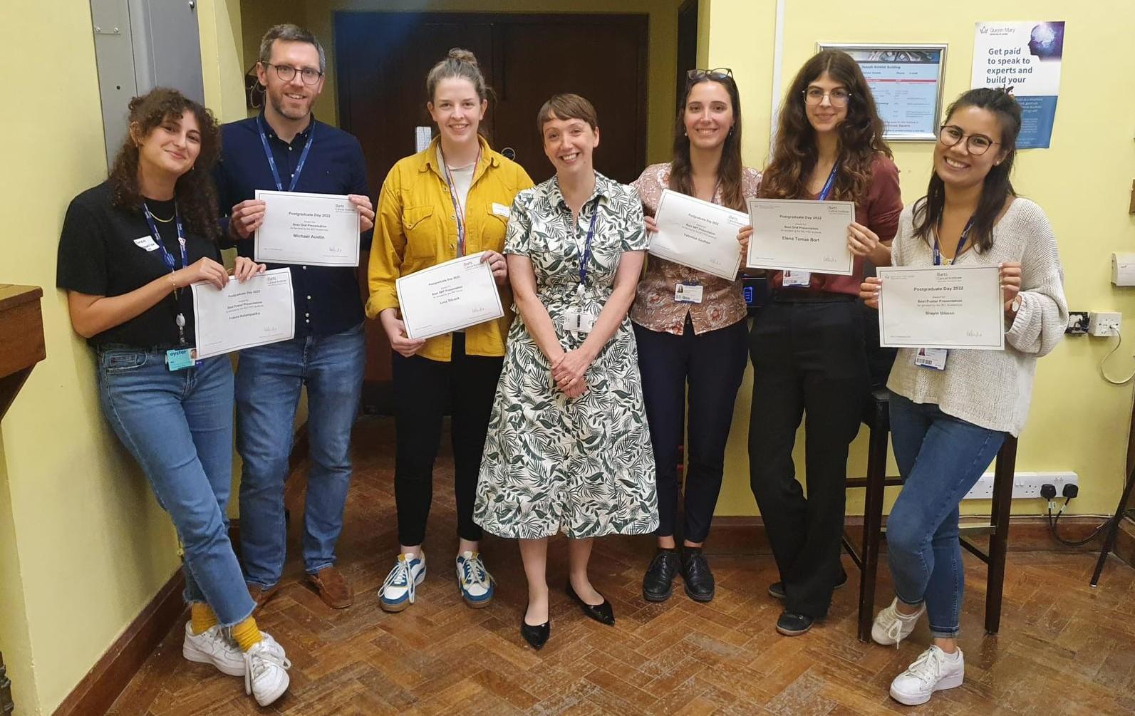 PhD students standing in a row holding up their award certificates.